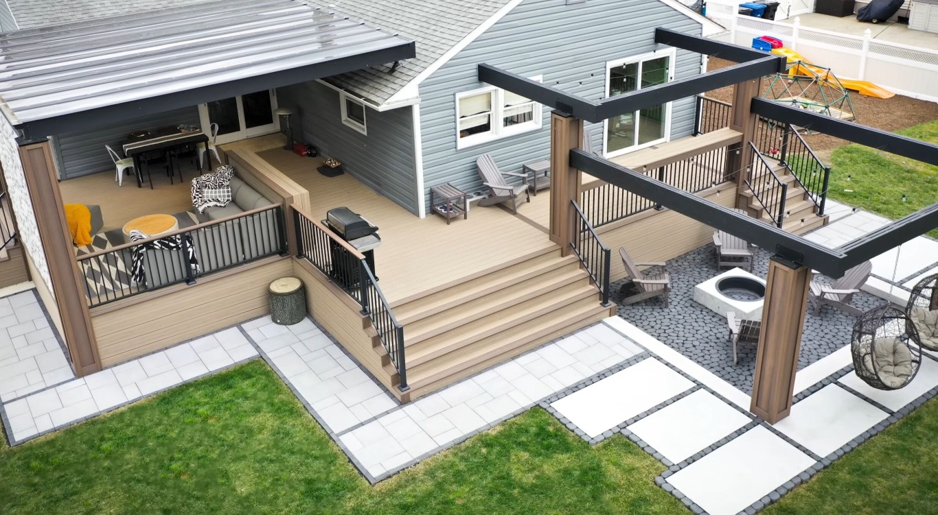 Aerial view of large multi-level composite deck with black railings attached to house with patio and landscaping